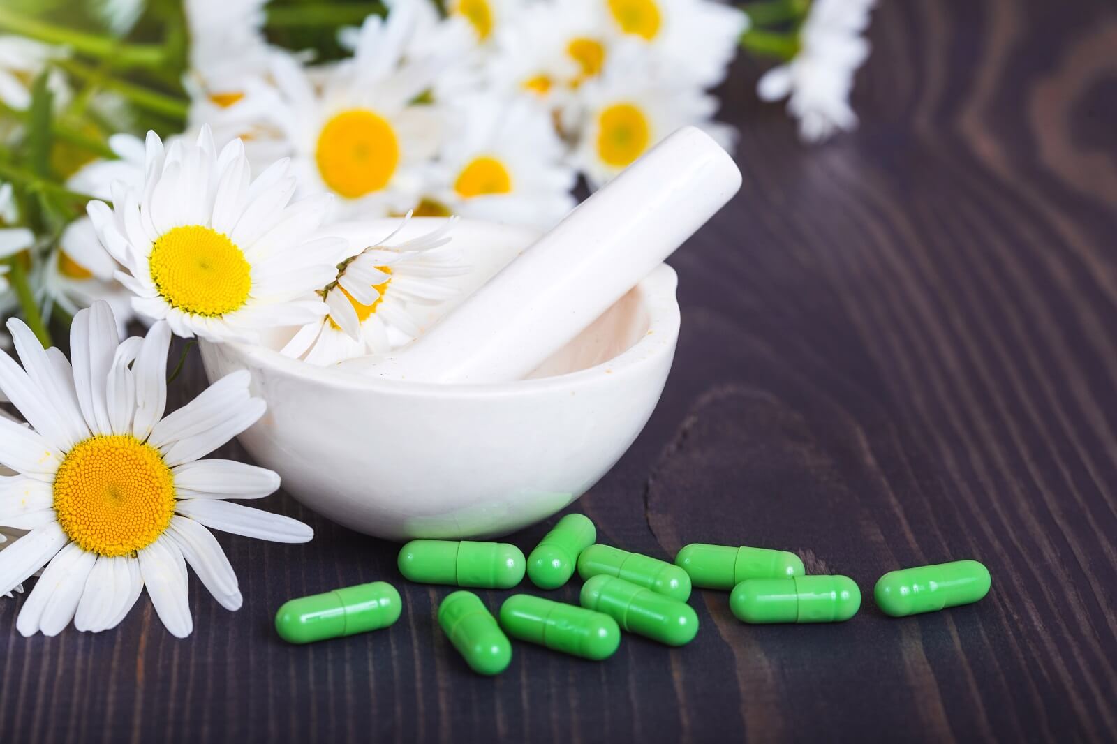 Chamomile flowers, white mortar and pestle, and green phytotherapeutic capsules